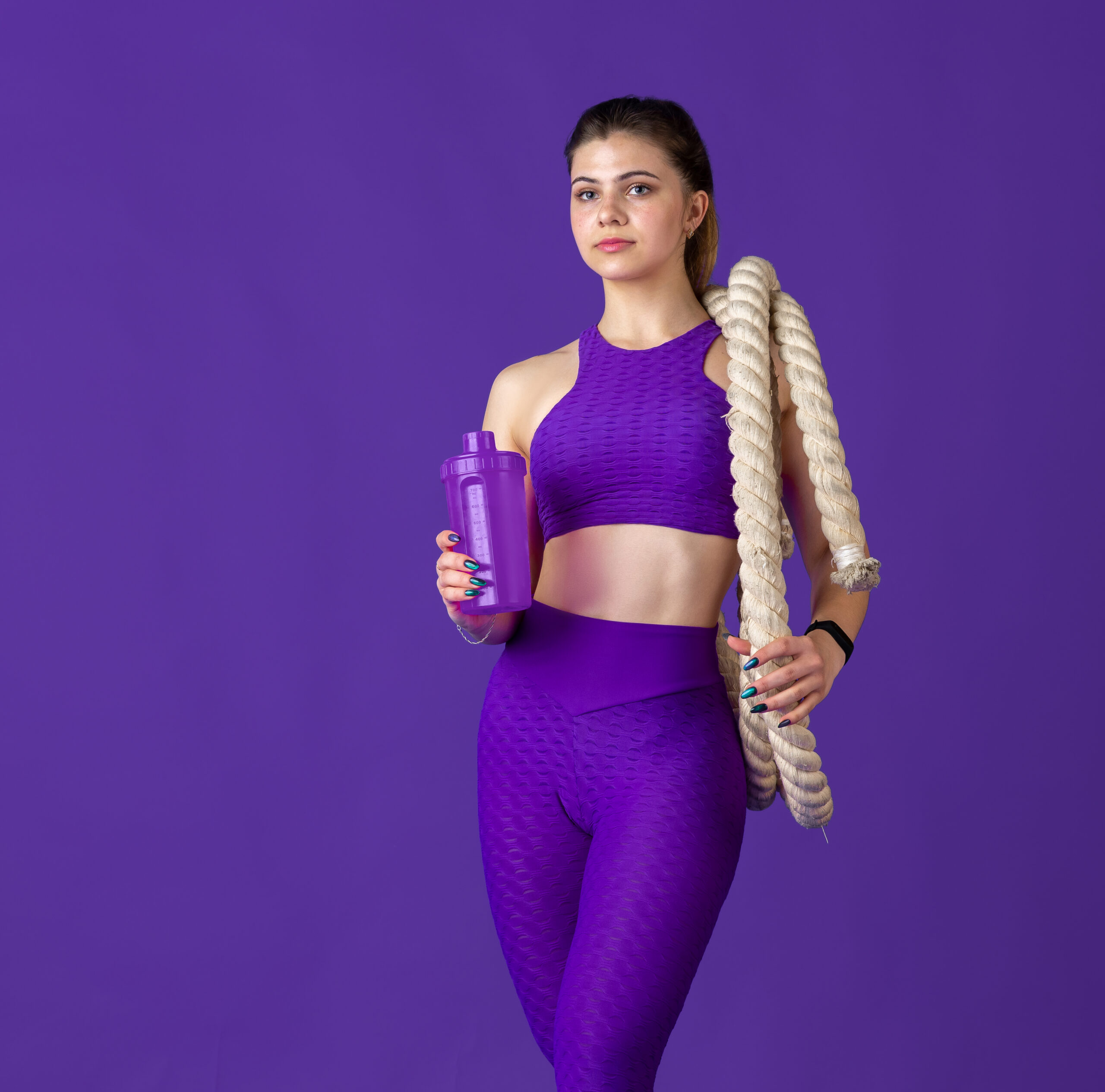 Beautiful young female athlete practicing on purple studio background, monochrome portrait